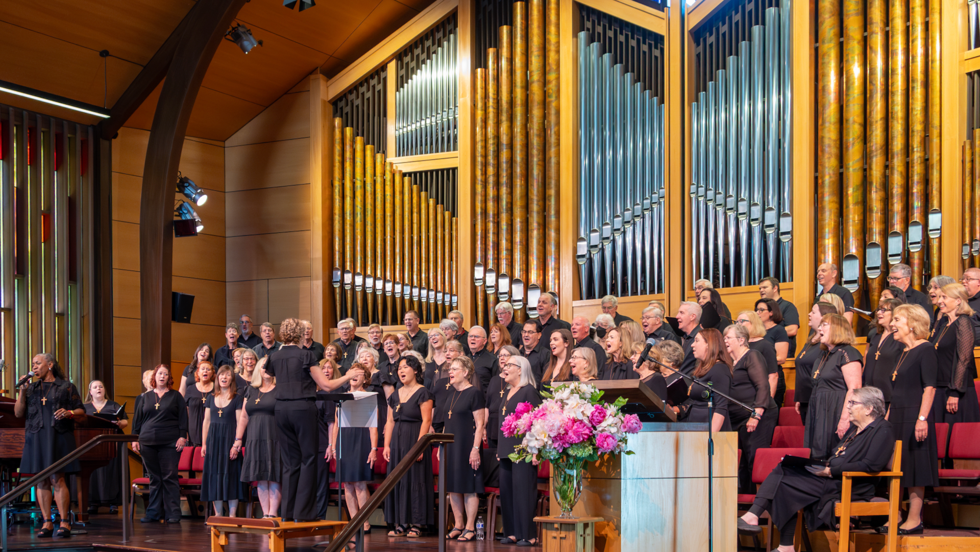 a choir and orchestra on stage with organ pipes in the background
